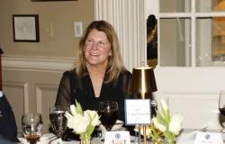 A woman with long dirty blonde hair sitting at a table. She is smiling and happy.